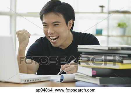 Picture - Young adult looking at laptop, smiling, making a fist. Fotosearch