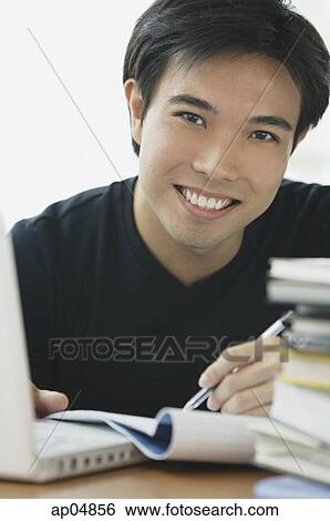Young adult smiling at camera, laptop and books next to him View Large Photo Image Stock Photograph - Young adult smiling at camera, laptop and books next to him. Fotosearch