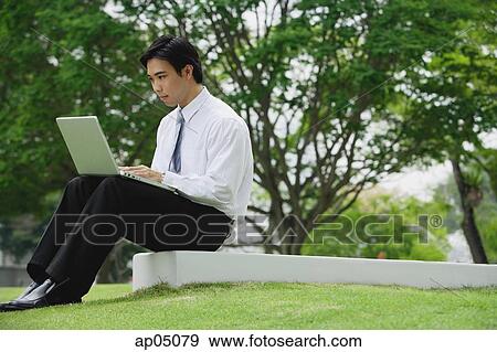 Stock Photo - Young businessman sitting in park using laptop. Fotosearch