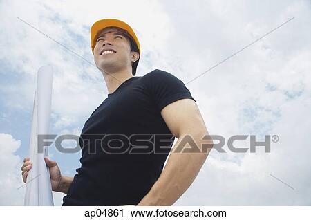 Young man in hardhat, carrying blueprints, smiling View Large Photo Image Stock Image - Young man in hardhat, carrying blueprints, smiling. Fotosearch