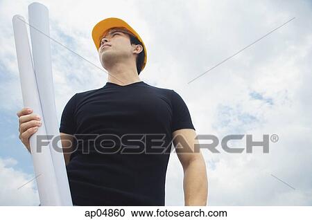 Young man wearing hardhat, carrying blueprints, outdoors View Large Photo Image Stock Image - Young man wearing hardhat, carrying blueprints, outdoors. Fotosearch