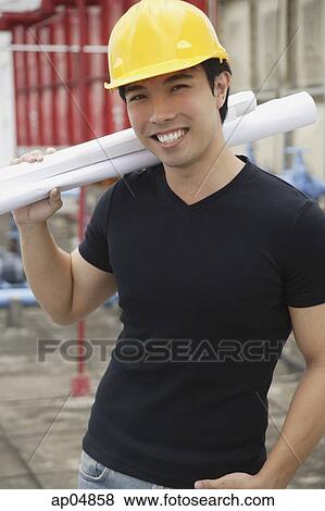 Stock Photo - Young man wearing hardhat, carrying blueprints. Fotosearch