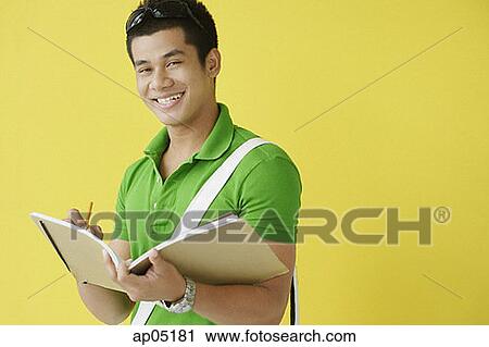 Young man writing in notebook, looking at camera View Large Photo Image Stock Image - Young man writing in notebook, looking at camera. Fotosearch