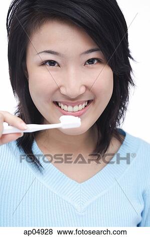 Stock Photo - Young woman brushing teeth, smiling at camera. Fotosearch