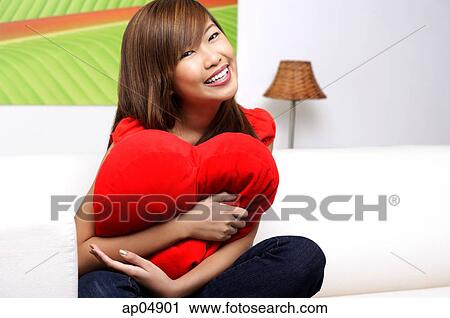 Stock Image - Young woman embracing pillow, smiling at camera. Fotosearch
