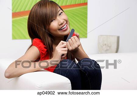 Young woman filing her nails, smiling at camera View Large Photo Image Stock Image - Young woman filing her nails, smiling at camera. Fotosearch