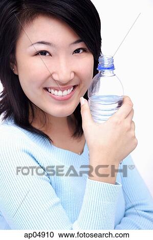 Young woman holding bottle of water, smiling at camera View Large Photo Image Stock Image - Young woman holding bottle of water, smiling at camera. Fotosearch