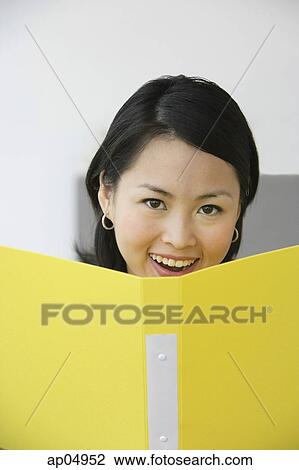 Stock Image - Young woman holding folder, smiling at camera. Fotosearch
