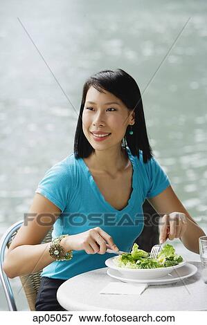 Stock Photo - Young woman in cafe, having salad, looking away. Fotosearch
