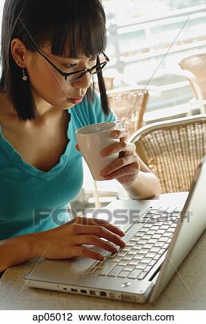 Young woman in cafe, holding cup and using laptop View Large Photo Image Stock Image - Young woman in cafe, holding cup and using laptop. Fotosearch
