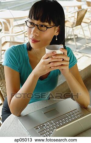 Young woman in cafe, holding cup, laptop on table next to her, looking away View Large Photo Image Stock Image - Young woman in cafe, holding cup, laptop on table next to her, looking away. Fotosearch