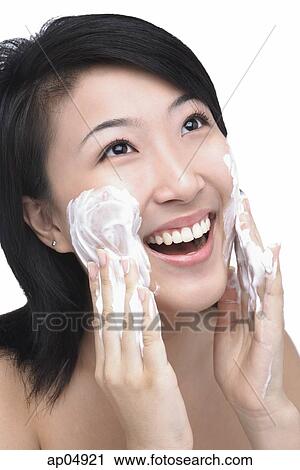 Stock Image - Young woman putting facial cleanser on her face. Fotosearch