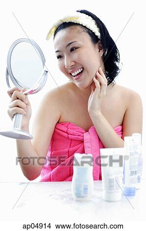 Young woman sitting at dressing table, looking in mirror, hand on chin View Large Photo Image Picture - Young woman sitting at dressing table, looking in mirror, hand on chin. Fotosearch