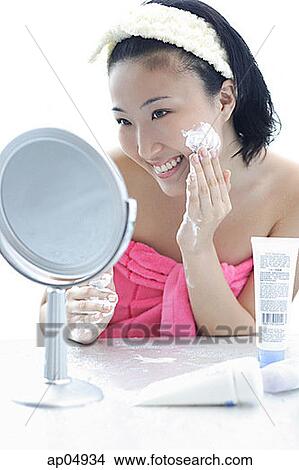 Young woman sitting at dressing table, putting lotion on face View Large Photo Image Picture - Young woman sitting at dressing table, putting lotion on face. Fotosearch