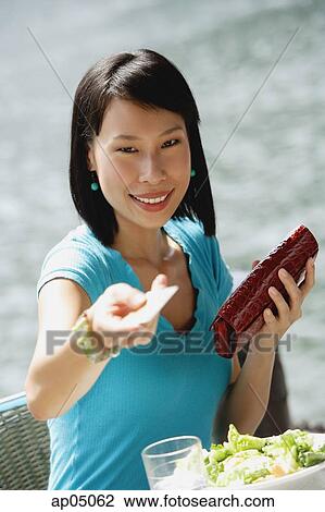 Young woman sitting at riverside cafe, holding credit card towards camera, smiling View Large Photo Image Stock Image - Young woman sitting at riverside cafe, holding credit card towards camera, smiling. Fotosearch