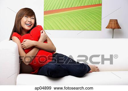 Young woman sitting on sofa, embracing pillow View Large Photo Image Stock Photo - Young woman sitting on sofa, embracing pillow. Fotosearch