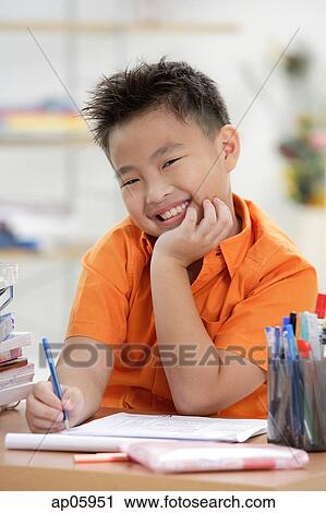 Stock Image - Boy doing homework, smiling at camera, hand on chin. Fotosearch