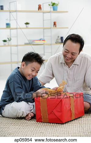 Picture - Boy opening gift box, father next to him. Fotosearch
