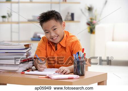 Boy sitting at desk doing homework, smiling at camera, portrait View Large Photo Image Stock Photo - Boy sitting at desk doing homework, smiling at camera, portrait. Fotosearch