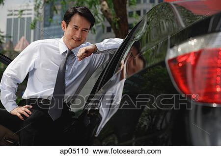 Businessman leaning on car, smiling View Large Photo Image Stock Image - Businessman leaning on car, smiling. Fotosearch