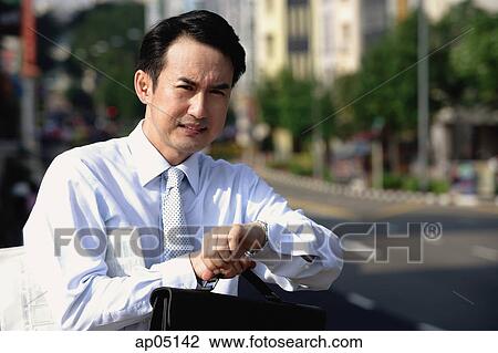 Stock Image - Businessman looking at watch, frowning. Fotosearch