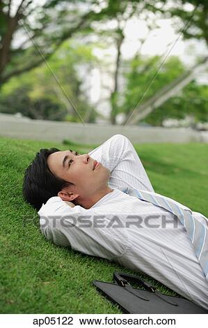Businessman lying on grass in park, looking up View Large Photo Image Stock Image - Businessman lying on grass in park, looking up. Fotosearch