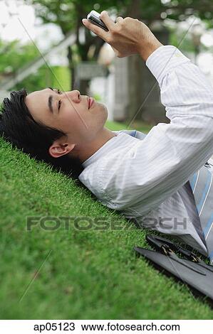 Businessman lying on grass in park, looking at mobile phone View Large Photo Image Stock Image - Businessman lying on grass in park, looking at mobile phone. Fotosearch