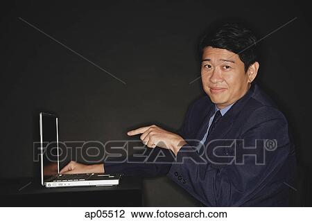 Businessman pointing at laptop, looking at camera View Large Photo Image Stock Image - Businessman pointing at laptop, looking at camera. Fotosearch