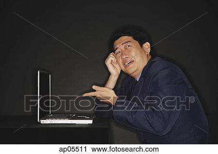 Stock Image - Businessman pointing at laptop next to him. Fotosearch