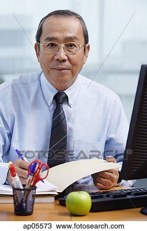 Businessman sitting at his desk, looking at camera View Large Photo Image Stock Image - Businessman sitting at his desk, looking at camera. Fotosearch