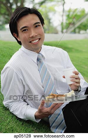 Businessman sitting in park, having take away lunch, looking at camera View Large Photo Image Stock Photo - Businessman sitting in park, having take away lunch, looking at camera. Fotosearch