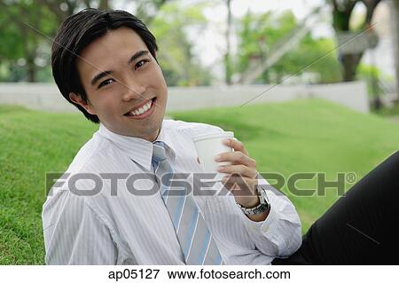 Businessman sitting in park, holding disposable cup View Large Photo Image Stock Photo - Businessman sitting in park, holding disposable cup. Fotosearch