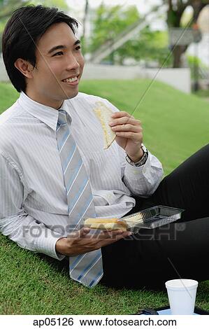 Businessman sitting on grass in park, having sandwich lunch View Large Photo Image Stock Photograph - Businessman sitting on grass in park, having sandwich lunch. Fotosearch