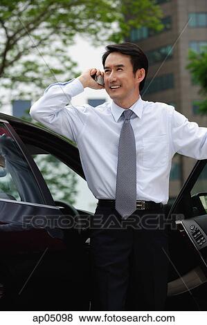 Stock Photo - Businessman standing next to car, using mobile phone. Fotosearch