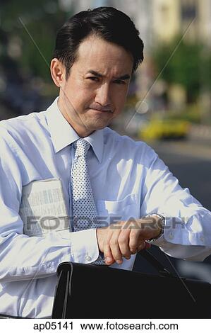 Businessman with newspaper under his arm, looking at watch, frowning View Large Photo Image Stock Image - Businessman with newspaper under his arm, looking at watch, frowning. Fotosearch