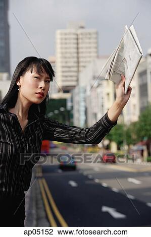 Stock Image - Businesswoman hailing a taxi with newspaper in hand. Fotosearch