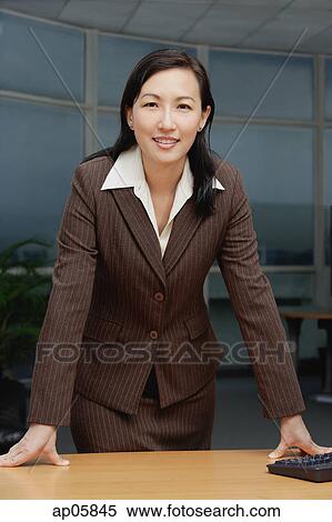Stock Photography - Businesswoman leaning on table, looking at camera. Fotosearch