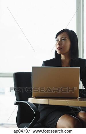 Businesswoman sitting at desk with laptop, looking away View Large Photo Image Stock Photo - Businesswoman sitting at desk with laptop, looking away. Fotosearch