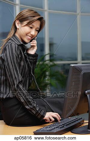 Businesswoman sitting on desk, using telephone View Large Photo Image Stock Photograph - Businesswoman sitting on desk, using telephone. Fotosearch