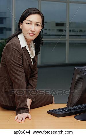 Businesswoman sitting on table, looking at camera View Large Photo Image Picture - Businesswoman sitting on table, looking at camera. Fotosearch