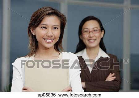 Businesswoman smiling at camera, another businesswoman in the background View Large Photo Image Stock Photograph - Businesswoman smiling at camera, another businesswoman in the background. Fotosearch