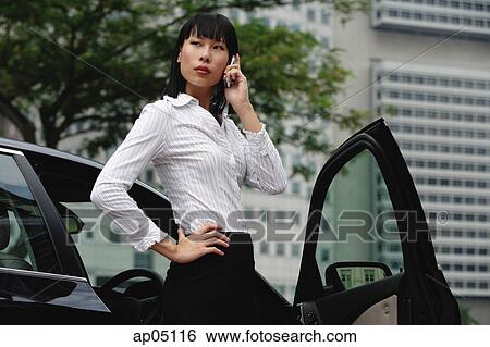 Businesswoman using mobile phone, standing next to car, hand on hip View Large Photo Image Stock Photograph - Businesswoman using mobile phone, standing next to car, hand on hip. Fotosearch