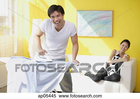 Couple at home, man ironing, woman sitting on sofa behind him View Large Photo Image Stock Photography - Couple at home, man ironing, woman sitting on sofa behind him. Fotosearch