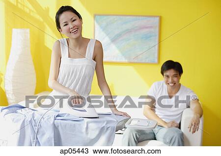 Couple at home, woman ironing, man sitting on sofa behind her, looking at camera View Large Photo Image Stock Image - Couple at home, woman ironing, man sitting on sofa behind her, looking at camera. Fotosearch