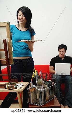 Stock Photo - Couple at home, woman painting on easel, man using laptop. Fotosearch