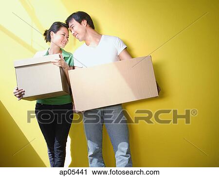 Couple carrying boxes, standing against yellow wall View Large Photo Image Stock Image - Couple carrying boxes, standing against yellow wall. Fotosearch