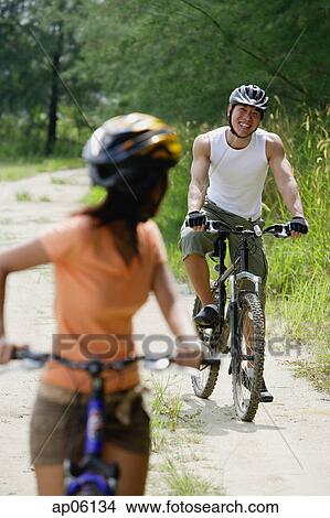Couple cycling, woman in foreground turning to look at man in the background View Large Photo Image Picture - Couple cycling, woman in foreground turning to look at man in the background. Fotosearch