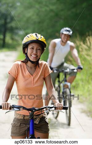Couple cycling, woman in foreground, looking at camera View Large Photo Image Stock Image - Couple cycling, woman in foreground, looking at camera. Fotosearch