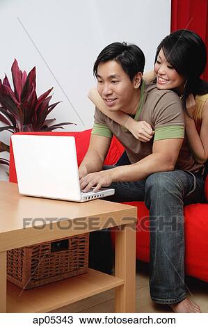 Couple in living room, looking at laptop View Large Photo Image Stock Image - Couple in living room, looking at laptop. Fotosearch