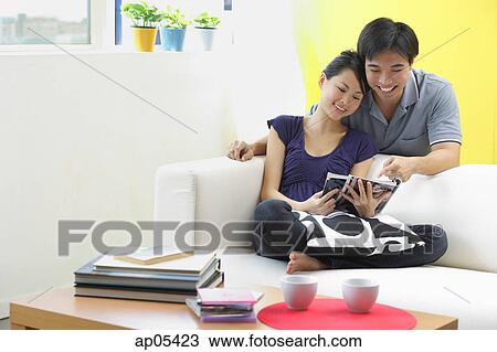 Couple in living room, looking at magazine View Large Photo Image Stock Image - Couple in living room, looking at magazine. Fotosearch